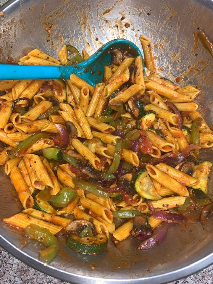 A pot of pasta with colorful vegetables and a serving spoon